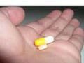 Iš arti rankos, laikančios geltoną ir baltą kapsulinę tabletę, primenančią mažą tabletę, paruoštą atlikti savo paskirtį.