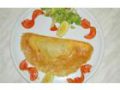 Baltoje lėkštėje dailiai sulankstytas omletą primenantis krepas su griežinėliais pjaustytais pomidorais, salotomis ir citrinos skiltele. Krepas yra aukso rudos spalvos, aplink jį dekoratyviai išdėlioti garnyrai.