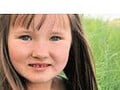 Stambiu planu jauna mergina ilgais rudais plaukais, švelniai besišypsanti žalios žolės ir šviesaus dangaus fone, akimis užsimenanti apie aukštą intelekto koeficientą.