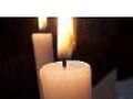 Iš arti dega balta žvakė su matoma liepsna, pastatyta tamsiame fone. Tolumoje matoma dar viena neryški žvakė, sukurianti šiltą ir ramią atmosferą, primenančią raminančią atmosferą, kurios dažnai ieškoma per depiliacijos vaškų užsiėmimus.