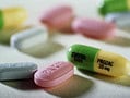 Iš arti įvairių tablečių ant paviršiaus. Viena yra žalia ir geltona kapsulė, pažymėta "Prozac 20 mg". Netoliese yra rožinės ir baltos spalvos tabletės, kai kuriose yra įspaustas tekstas. Šis asortimentas iliustruoja Lietuvoje dažniausiai tyrinėjamus „Maisto papildų“.
