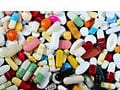 Didelis asortimentas spalvingų tablečių ir kapsulių, primenančių išbarstytą žymų kolekciją. Paveikslėlyje yra įvairių atspalvių raudonos, geltonos, baltos, mėlynos ir žalios įvairių formų ir dydžių vaistai.