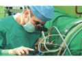 Chirurgas, vilkintis žalią chirurginį chalatą ir mėlyną kepuraitę, atlieka procedūrą. Jie yra susikaupę savo darbui, naudoja medicinos įrangą ir techniką. Įvykis vyksta ligoninės operacinėje.