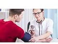 Sveikatos priežiūros specialistas, naudodamas sfigmomanometrą, tikrina paciento kraujospūdį. Pacientas, vilkintis raudonais marškiniais, sėdi, o profesionalas baltu medicininiu chalatu sutelkia dėmesį į matavimą – atsižvelgdamas į nebivololio arterinės hipertenzijos gydymą.