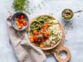 Lėkštė keptos lašišos su žaliosiomis pupelėmis ir kuskusu, prie kurios patiekiama nedidelė dubenėlė pomidorų salotų su pesto – tai patiekalas, atitinkantis sveikos mitybos principus.